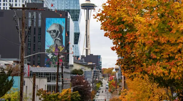 Seattle street photography captures a vibrant autumn scene with colorful trees, a mural, and the Space Needle in the distance.