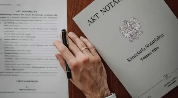 Akt poświadczenia dziedziczenia i umowa darowizny na biurku notariusza. Dłoń z obrączką trzyma długopis.