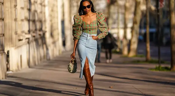 Mujer con top de cuadros y falda vaquera larga con abertura, botas altas y bolso.