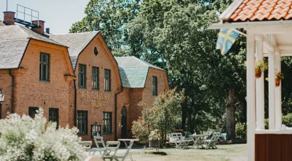 Vacker tegelbyggnad med texten "A-B. FORSVIKS BRUK". Utomhusbord och stolar inbjuder till avkoppling vid detta charmiga forsviks vandrarhem.