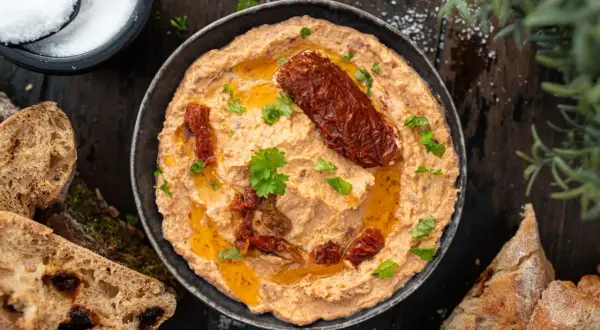 Cremiger Feta Dip mit sonnengetrockneten Tomaten, Olivenöl und frischer Petersilie, serviert mit knusprigem Brot.
