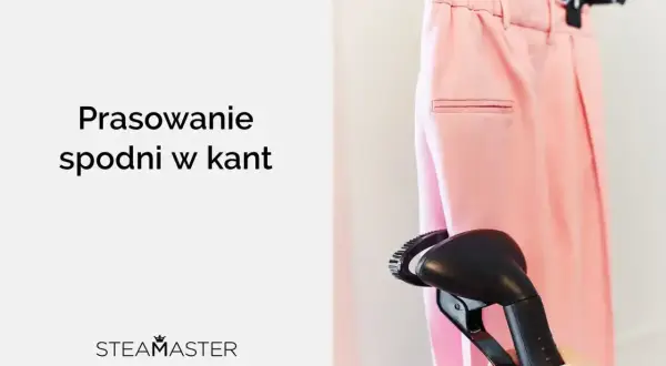 Różowe spodnie w kant wiszą na wieszaku, a ręka trzyma parownicę, gotową do prasowania.
