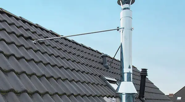 Edelstahl-Ofenrohre verbinden sich auf einem dunklen Ziegeldach. Ein Metallarm stützt das glänzende Rohr.