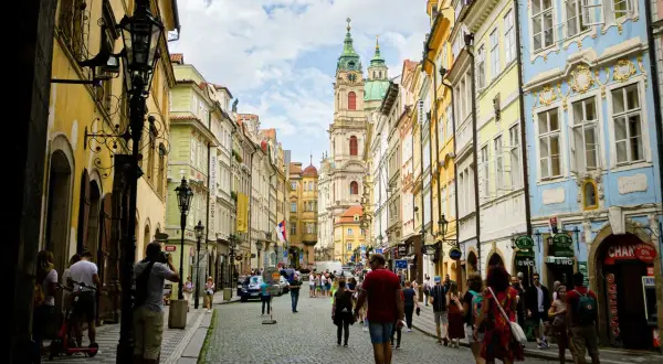 Rue pavée bordée de maisons colorées à Prague, avec une église baroque au loin. Une scène typique du top 10 des attractions de Prague.