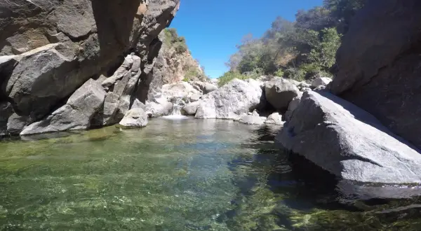 Agua cristalina en la charca de las nutrias, rodeada de rocas y vegetación bajo un cielo azul.