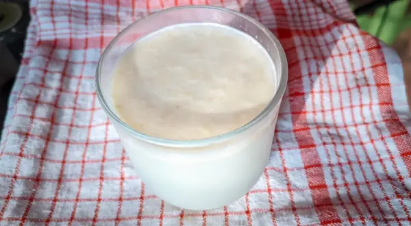 Szklanka z kremowym napojem, który może być kefir czy maślanka, stoi na czerwono-białym ręczniku.