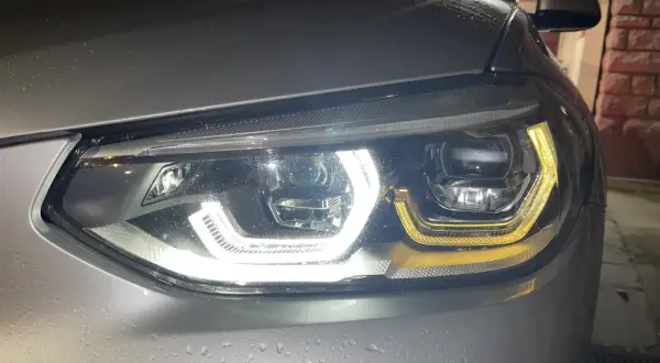 Gros plan sur un phare led qui clignote, illuminant la carrosserie mouillée d'une voiture argentée.