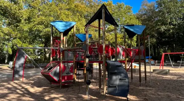 Ein bunter Spielplatz mit Klettergerüst und Schaukeln in einem der Wuppertal Parks, umgeben von Bäumen im Herbstlicht.