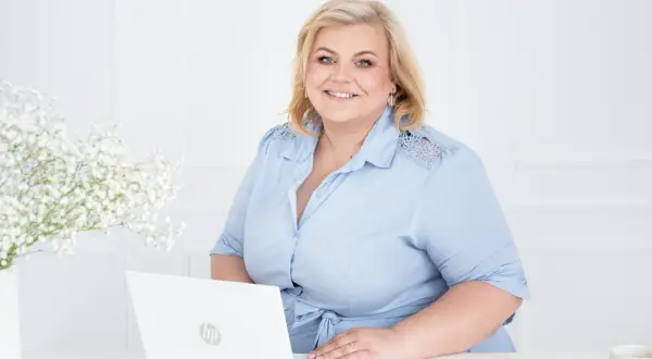 Uśmiechnięta kobieta przy laptopie, gotowa pomóc w znalezieniu pracy w Wielkiej Brytanii.