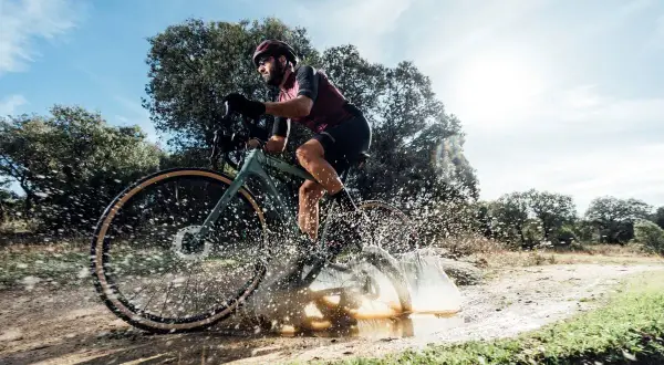 Ciclista en bici de gravel salpicando agua en un camino rural. ¡Así es el gravel!