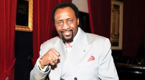 Thomas Hearns now, a boxing legend, smiles confidently in a light grey suit, red tie, and pocket square.