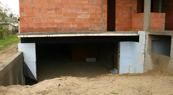 Budowa piwnicy: widok fundamentów i ścian z pustaków. Piasek wokół, widać izolację.