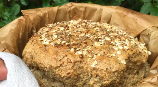 Pan de lino recién horneado, cubierto de semillas y avena, envuelto en papel de hornear.