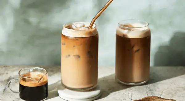 Deux verres de latte froid avec une paille dorée, un petit shot d'espresso et des grains de café.