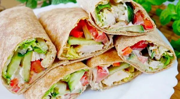 Pyszna tortilla z kurczakiem na ciepło, pełna świeżych warzyw: sałaty, pomidorów i ogórka. Idealna na szybki posiłek.