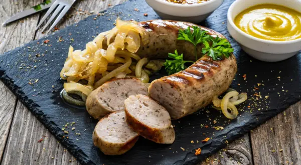 Pyszna biała kiełbasa z grilla, podana z duszonymi cebulkami i musztardą. Idealna na letni obiad.