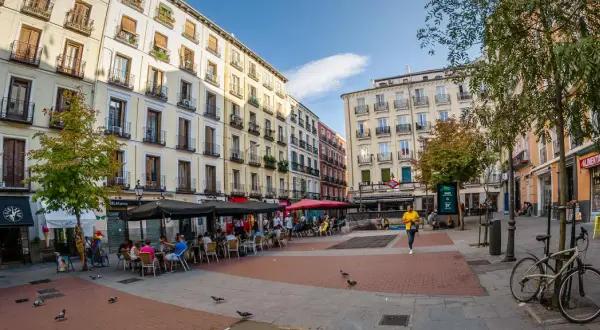 Piazza vivace con caffè all'aperto e persone che passeggiano, un'atmosfera tipica della zona gay di Madrid.