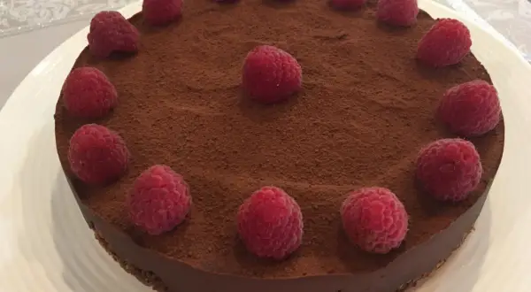 Tarte chocolat framboise, une gourmandise visuellement irrésistible, saupoudrée de cacao et ornée de framboises fraîches.