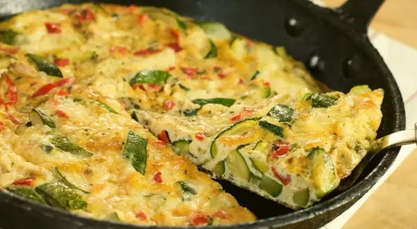 Pyszny omlet z cukinii z kawałkami papryki, podany na patelni. Idealny na śniadanie lub lekki obiad.