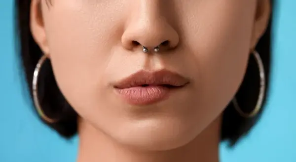 Kobieta z septum w nosie i kolczykami w uszach na niebieskim tle.