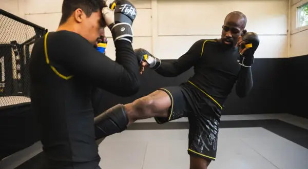 Deux athlètes s'entraînent en mma sport de combat. L'un porte des protège-tibias et donne un coup de pied, l'autre se protège la tête.