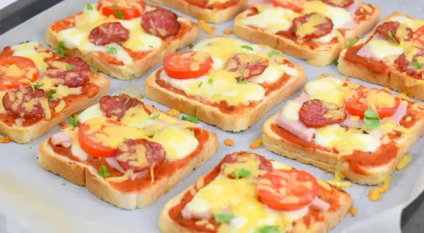 Pyszne pizza z chleba tostowego z serem, salami i pomidorkami, gotowa do pieczenia.