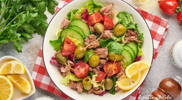 Insalata di tonno fresca e colorata con pomodori, cetrioli, olive e capperi, guarnita con limone.