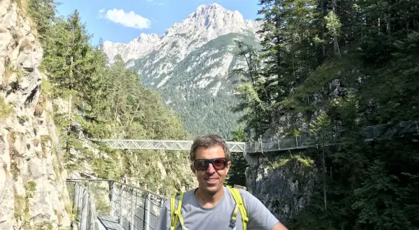 Mann auf einem Steg in der Leutascher Geisterklamm, umgeben von Felsen und Bäumen, mit majestätischen Bergen im Hintergrund.