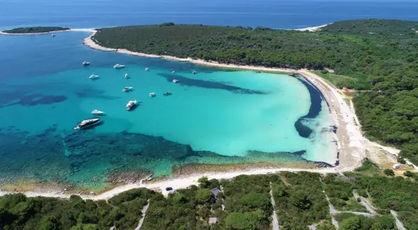 Widok z lotu ptaka na turkusową zatokę z łodziami, otoczoną zielonymi lasami. To musi być najpiękniejsza plaża w Chorwacji!