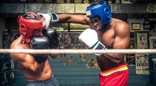 Två boxare i ringen, en med röd och en med blå hjälm, tränar funktionell fitness.