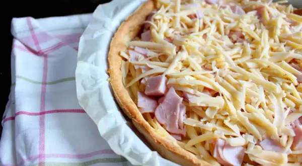 Tarta z szynką i serem, gotowa do pieczenia. Kruche ciasto, kawałki szynki i obfita warstwa startego sera.
