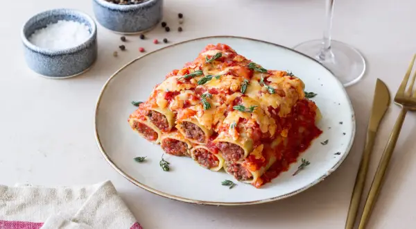 Pyszne cannelloni z mięsem mielonym, zapieczone pod sosem pomidorowym i serem, udekorowane świeżym tymiankiem.