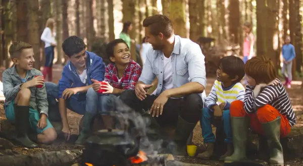 Kinder lachen und trinken am Lagerfeuer. Ein Lehrer verweigert die Klassenfahrt, aber die Kinder genießen den Ausflug trotzdem.