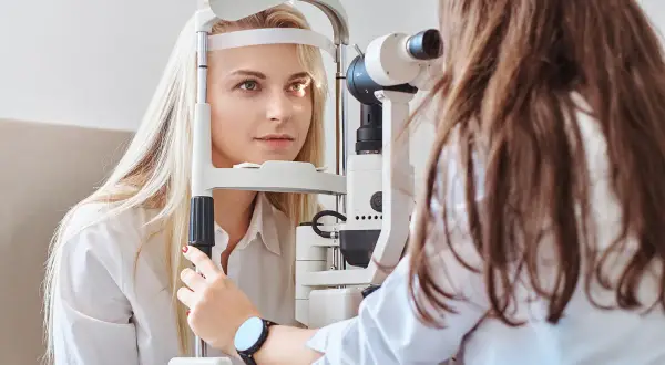 Badanie wzroku u okulisty. Pacjentka z jasnymi włosami poddaje się badaniu, które może pomóc zdiagnozować męty w oku, czasem pojawiające się po wysiłku fizycznym.