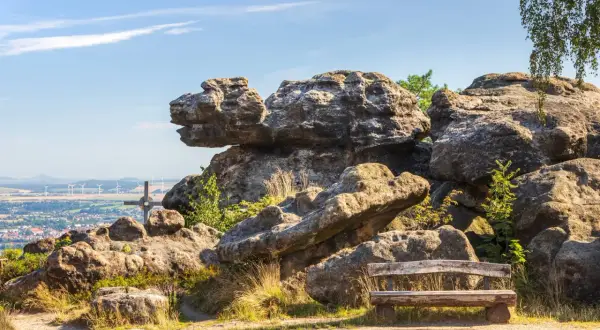 Ein Holzbank lädt zum Verweilen ein, mit Blick auf bizarre Felsen im Zittauer Gebirge und eine Stadt in der Ferne.