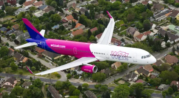 Różowy samolot Wizzair przelatuje nad osiedlem domów jednorodzinnych.