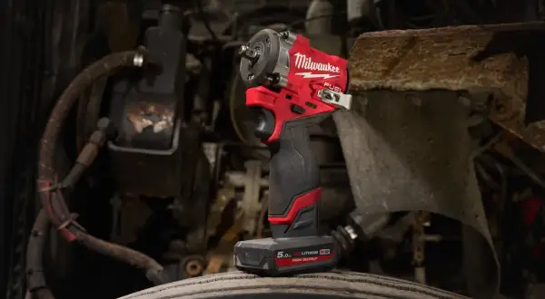 Czerwony klucz udarowy Milwaukee M12 FUEL stoi na oponie, gotowy do pracy przy silniku.