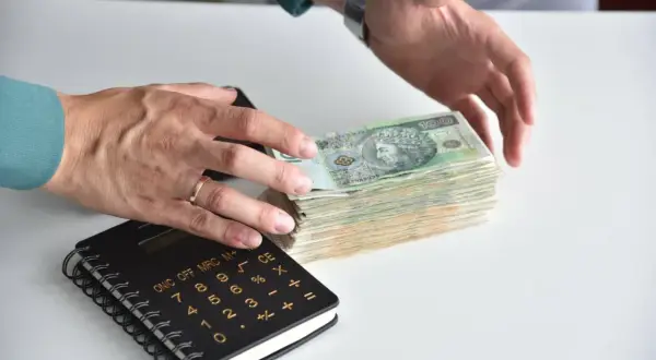 Ręce liczą stos banknotów, obok kalkulator. Jak odzyskać pieniądze z banku po zmarłej osobie?
