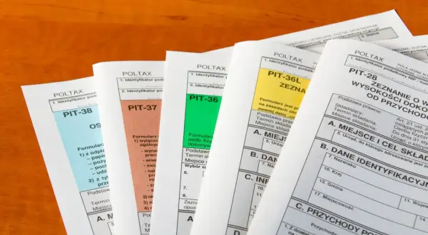 Różne formularze PIT (PIT-38, PIT-37, PIT-36, PIT-36L, PIT-28) leżą na drewnianym blacie. Czy trzeba rozliczać PIT-11?