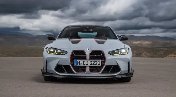 Szare BMW M4 CS z czerwonymi akcentami i agresywnym grillem, gotowe do jazdy po pustynnej drodze pod burzowym niebem.