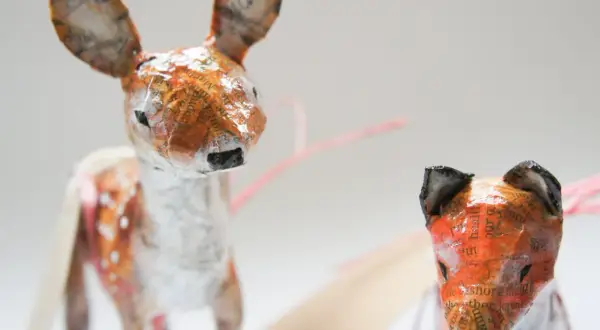 Urocze figurki z papier mache: jelonek w plamki i lis. Ich uszy zdobią fragmenty tekstu.