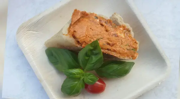 Ein Stück Brot mit leckerer Tomatenbutter, garniert mit frischem Basilikum und einer Kirschtomate. Perfekt zum Tomatenbutter selber machen.