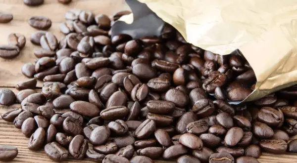Chicchi di caffè Arabica tostati, con un sacchetto dorato aperto da cui fuoriescono. Il caffè Arabica, noto per il suo aroma delicato, è il significato di un'esperienza gustativa raffinata.