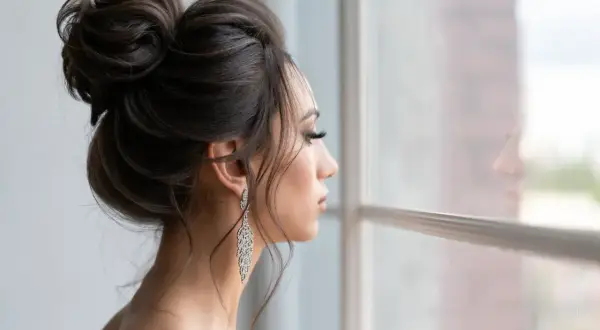 Elegancka fryzura wieczorowa z upiętymi włosami i długimi, błyszczącymi kolczykami. Kobieta patrzy przez okno, marząc o balu.