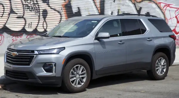 Szary Chevrolet Traverse SUV zaparkowany przed ścianą z graffiti.
