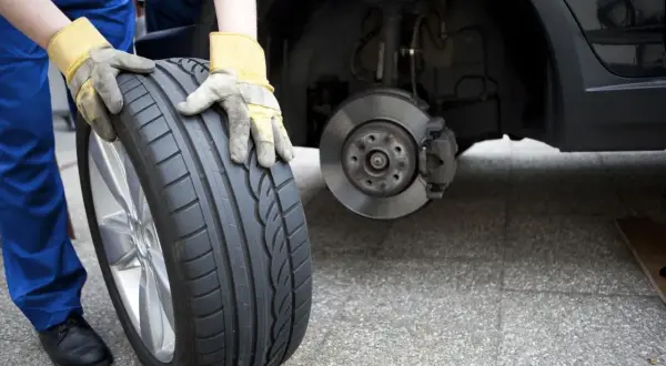 Mechanik w żółtych rękawicach trzyma nowe opony, zastanawiając się, czy lepsze opony na przód czy tył zapewnią bezpieczeństwo.