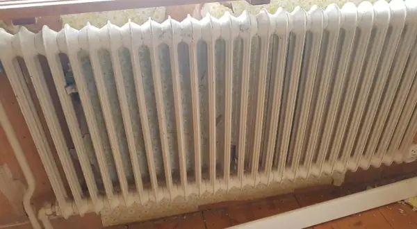 Gammal vit element med blommig tapet bakom. Kanske dags att ta bort elementet och tapeten för en renovering.