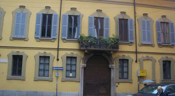 Facciata gialla del **Palazzo Belgioioso** con finestre dalle persiane azzurre e un balcone fiorito.