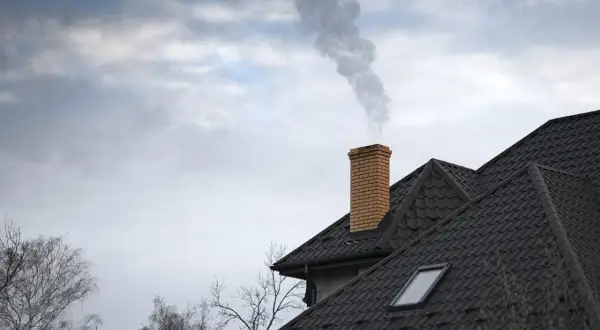 Dym wydobywa się z ceglanego komina na dachu domu.