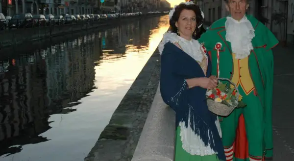 Coppia in costume tradizionale, una maschera milanese, passeggia lungo un naviglio al tramonto.
